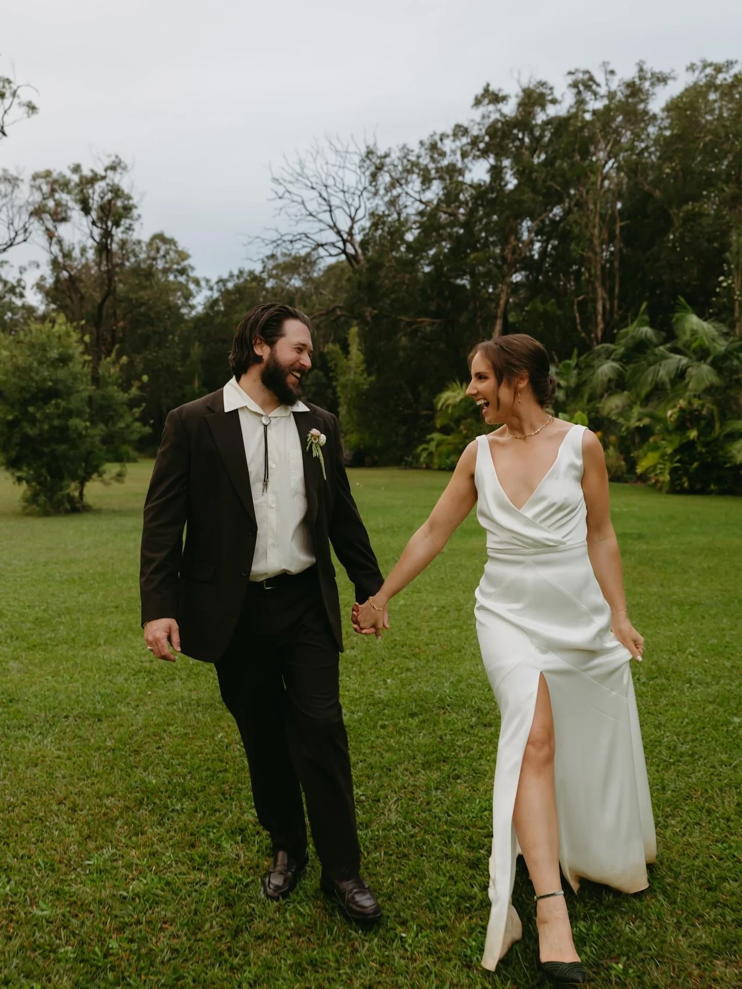 A bride and groom holding hands and smiling at each other outdoors on a grassy field with trees in the background.| Goolawah Retreat Wedding Crescent Head