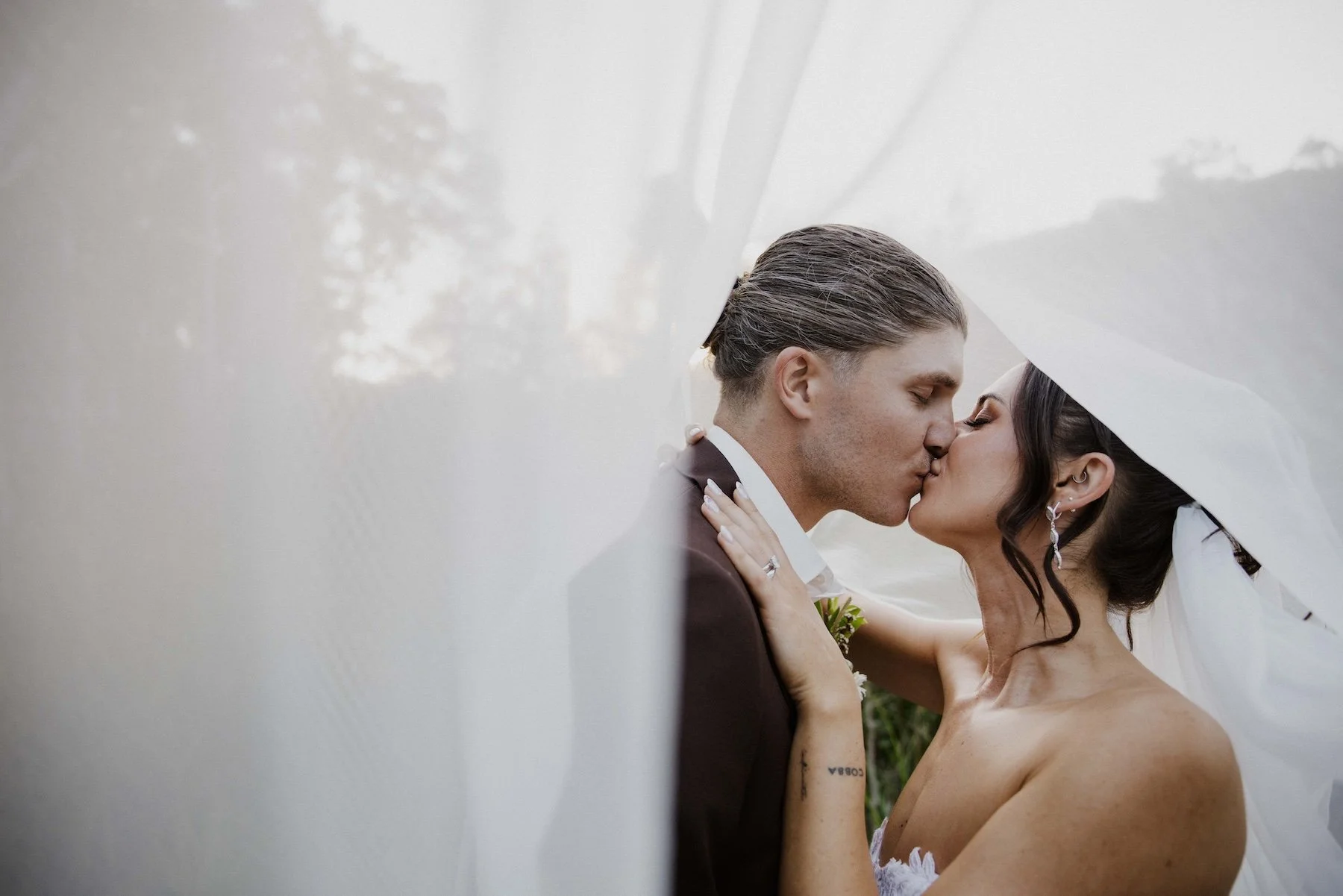 | Goolawah Retreat Wedding Crescent Head A bride and groom kissing under a white veil on their wedding day.