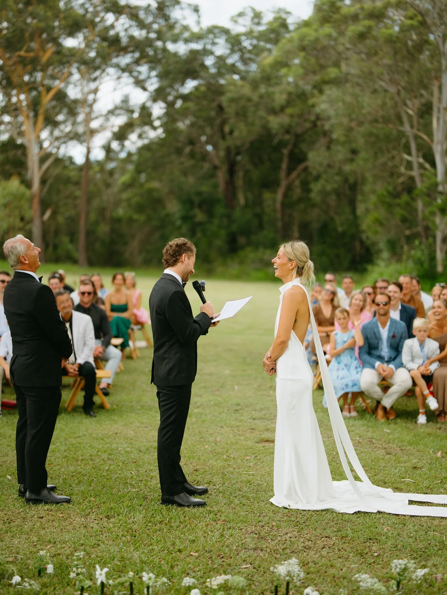 A wedding ceremony outdoors with a couple exchanging vows, surrounded by seated guests, trees, and grass.| Goolawah Retreat Wedding Crescent Head