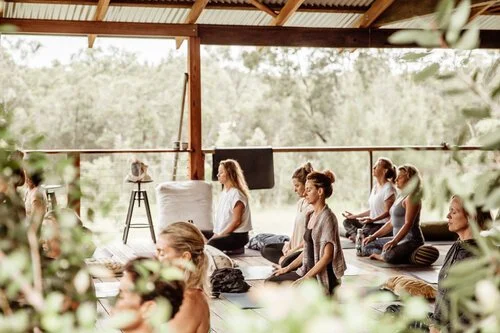 Women meditating in a peaceful, open-air studio surrounded by greenery