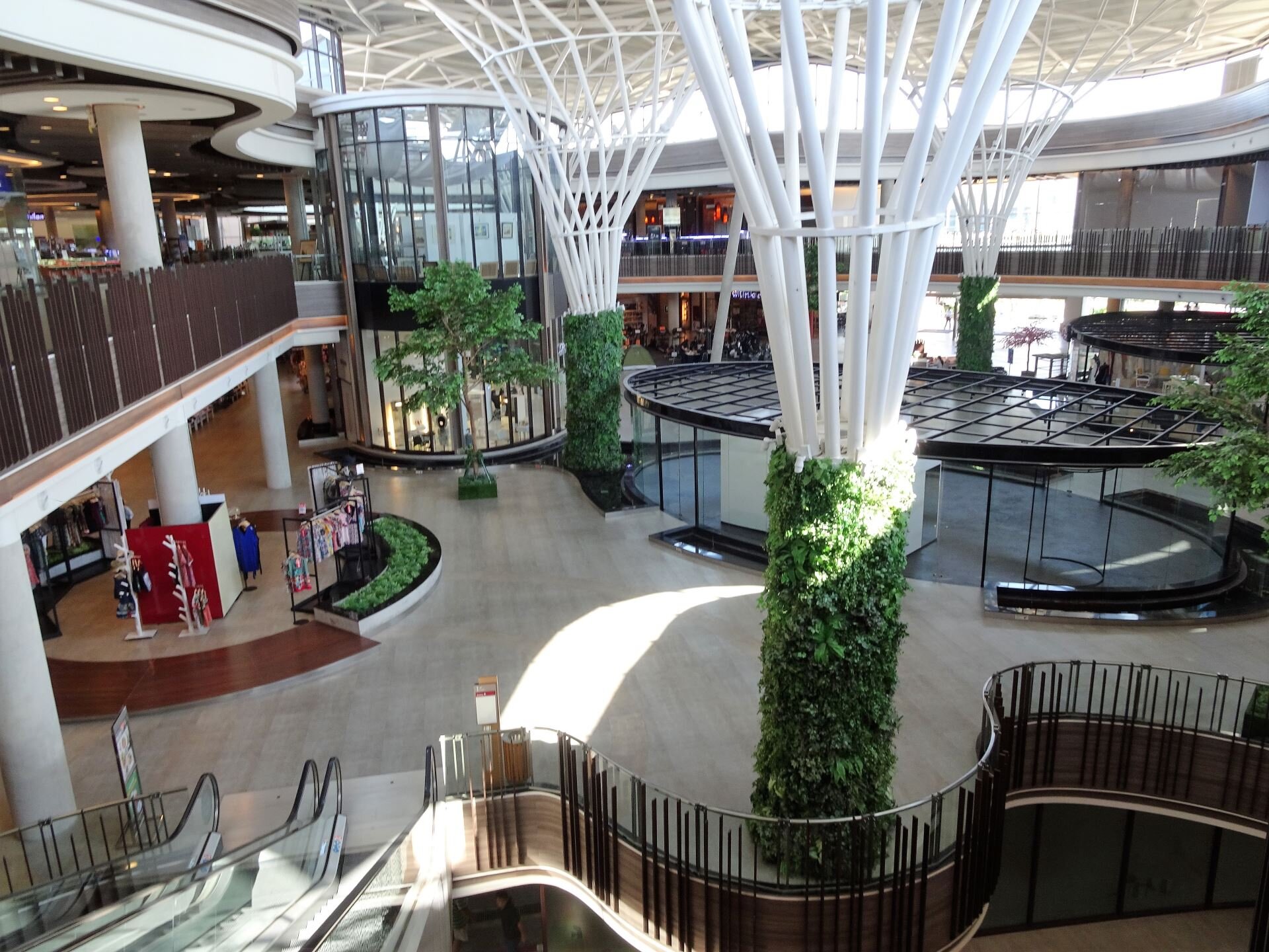 Chiang Mai shopping mall interior with escalators, glass roof, vertical garden columns, and retail displays.