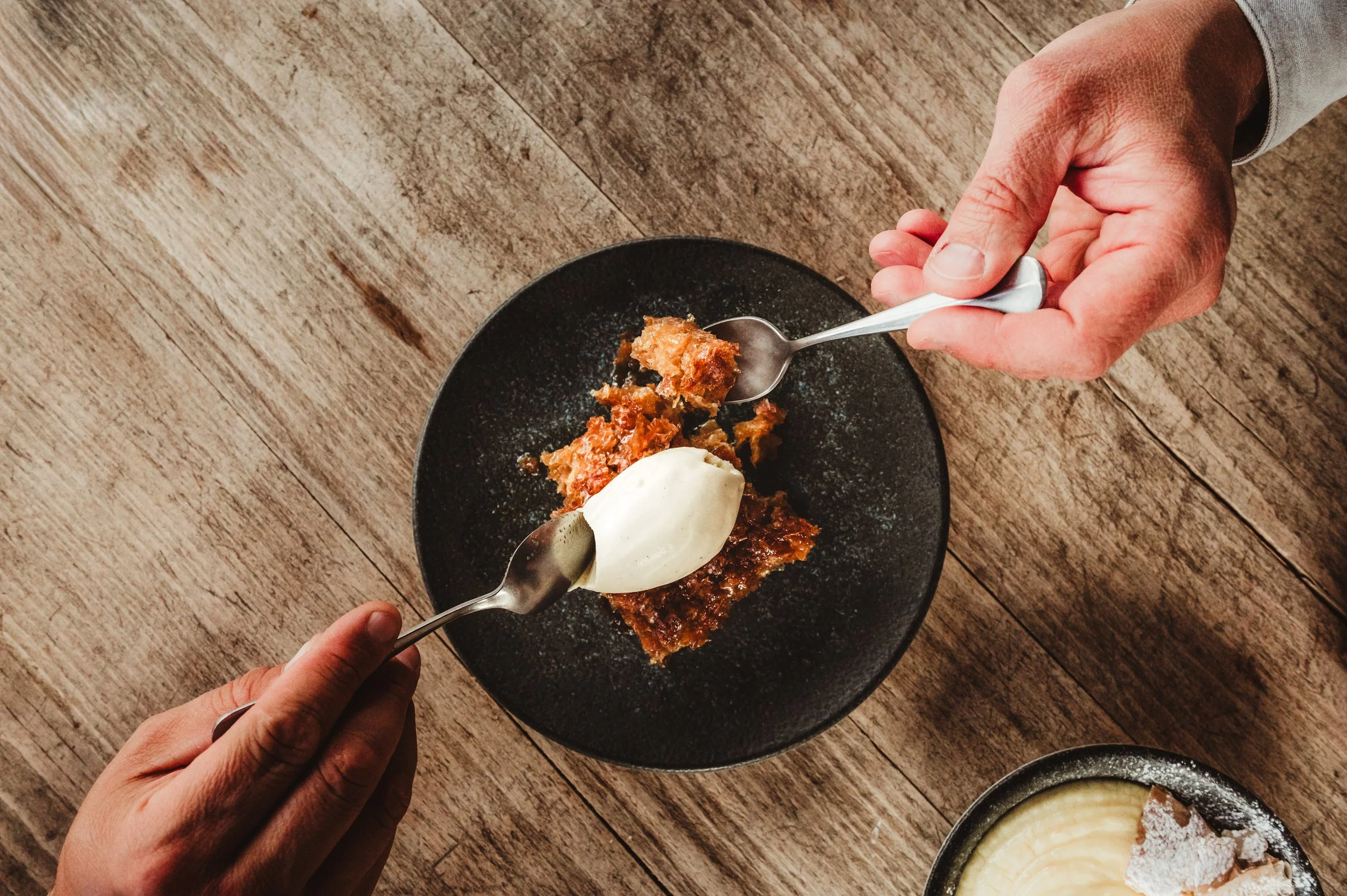 Griechisches Dessert von oben fotografiert zwei Hände mit Löffel nehmen sich ein Stück davon.