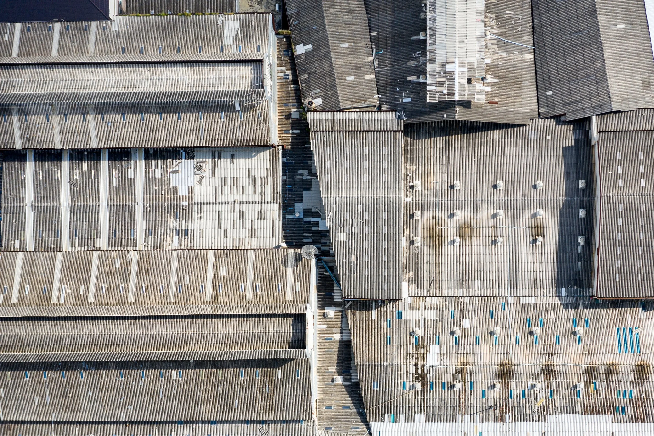 Aerial view of densely packed industrial buildings with weathered corrugated metal roofs, skylights, vents, and rooftop equipment.
