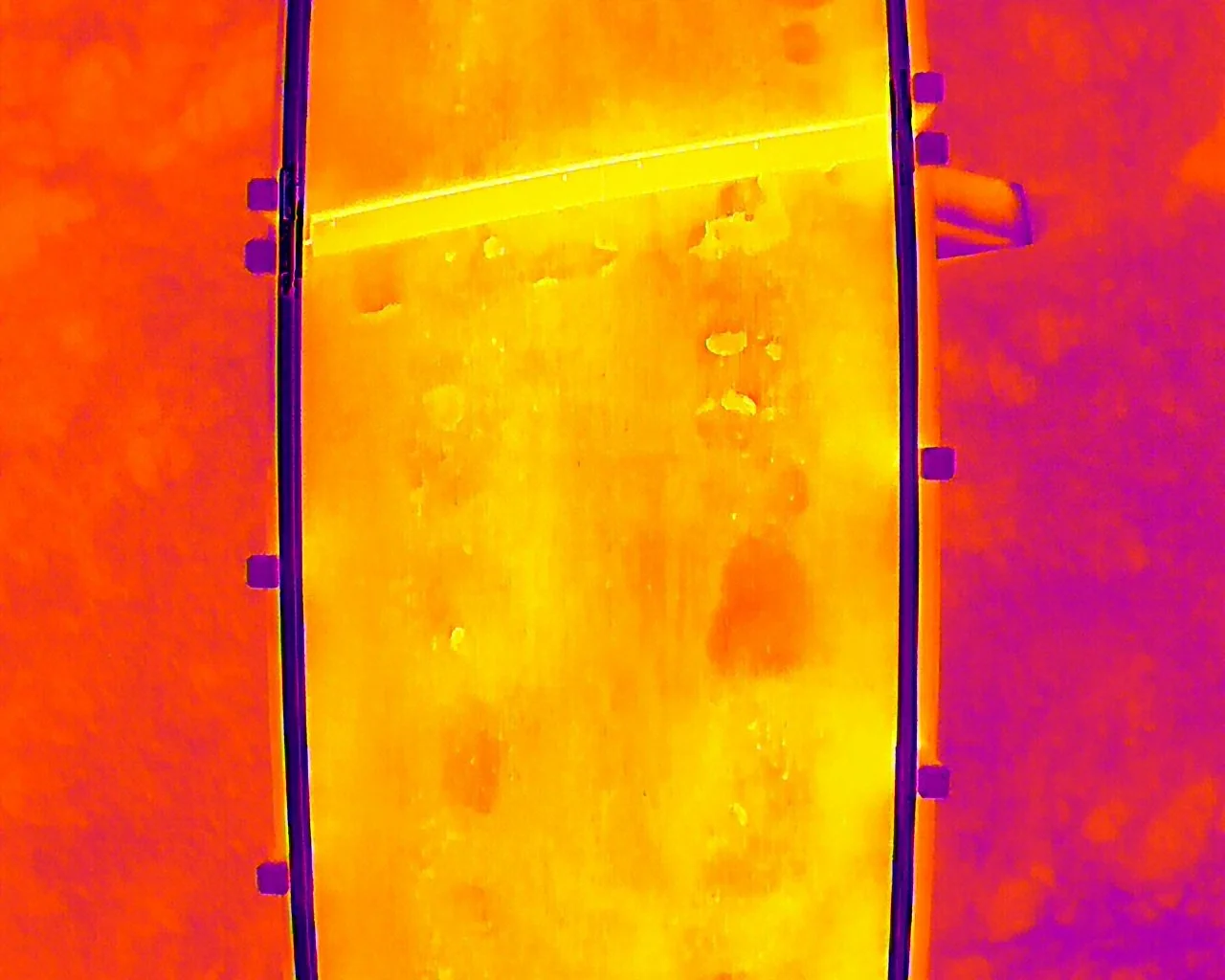 Thermal imaging view of a metal door or panel with bright heat patterns and dark hinges