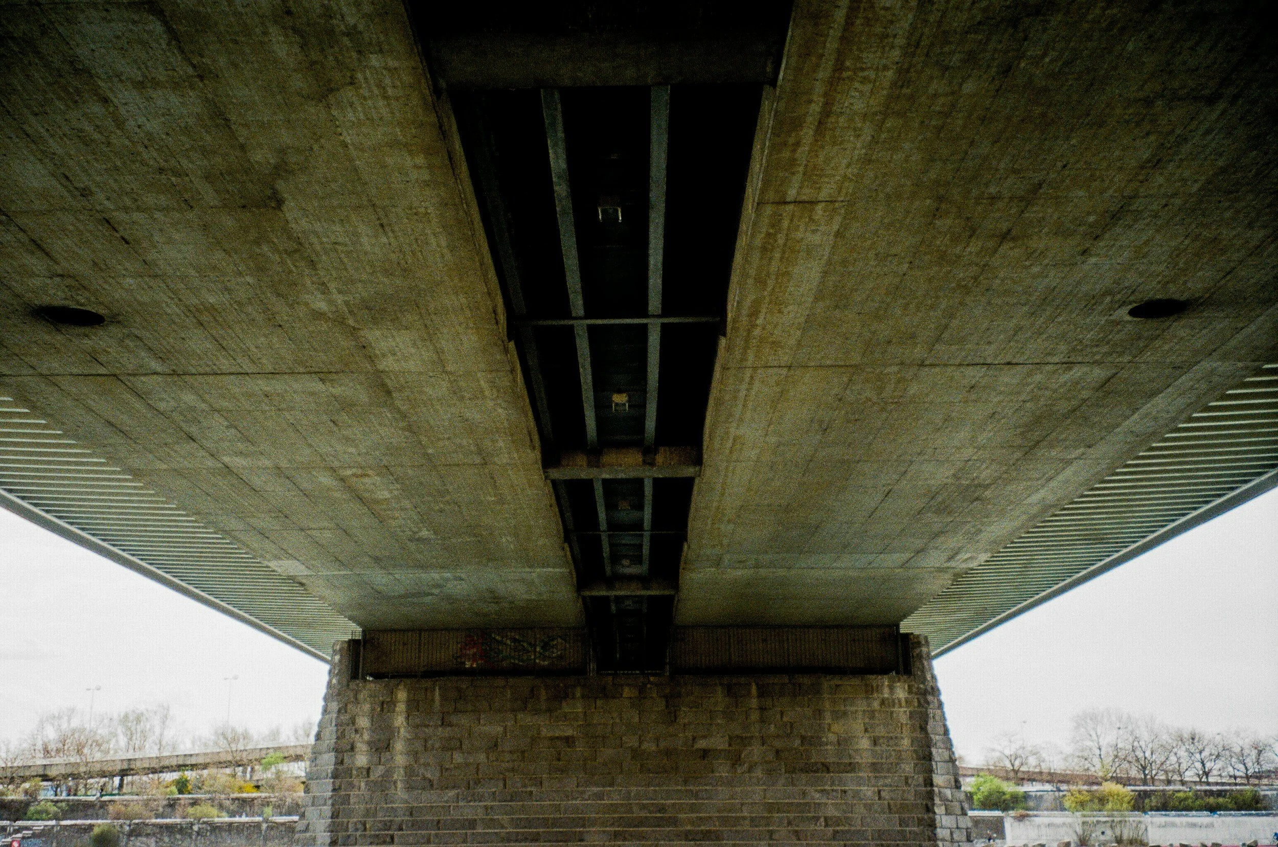 View from beneath a large concrete highway overpass supported by a stone-clad pillar.