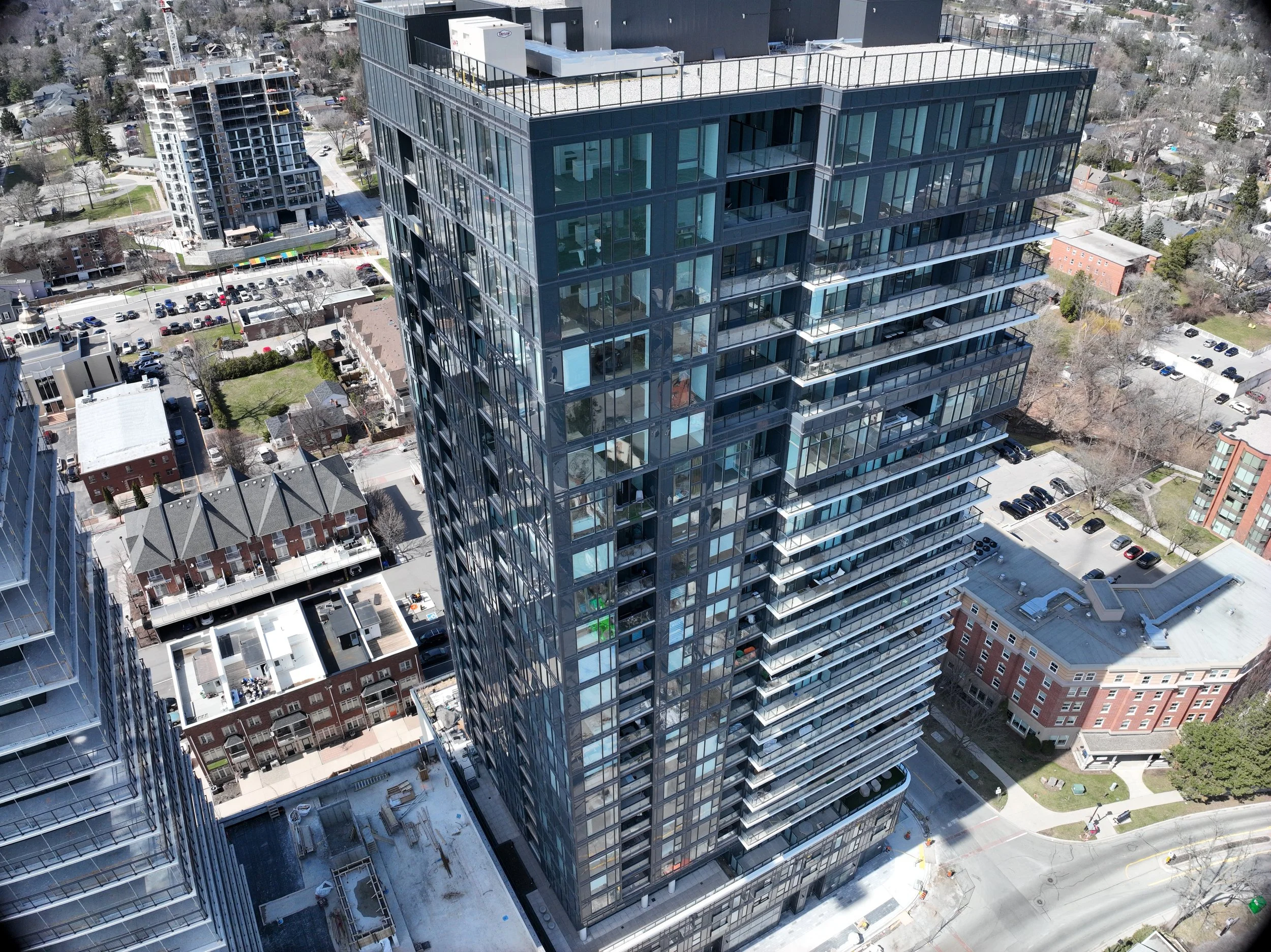 Aerial view of a modern high-rise residential building with glass balconies surrounded by urban streets, parked cars, and neighboring buildings. burlington ontario aerial roof and building envelope inspections service