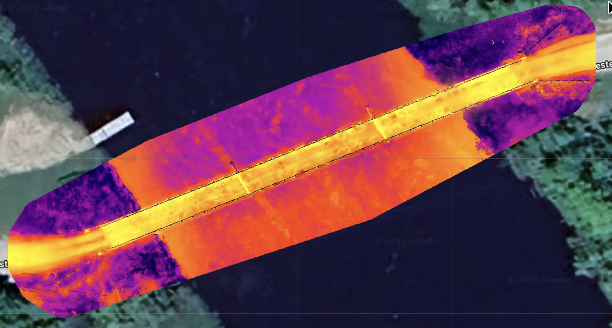 False-color aerial thermal image of a bridge crossing a dark river, with surrounding vegetation and roadways. manitoba bridge and infrastructure aerial roof and building envelope thermal inspections service