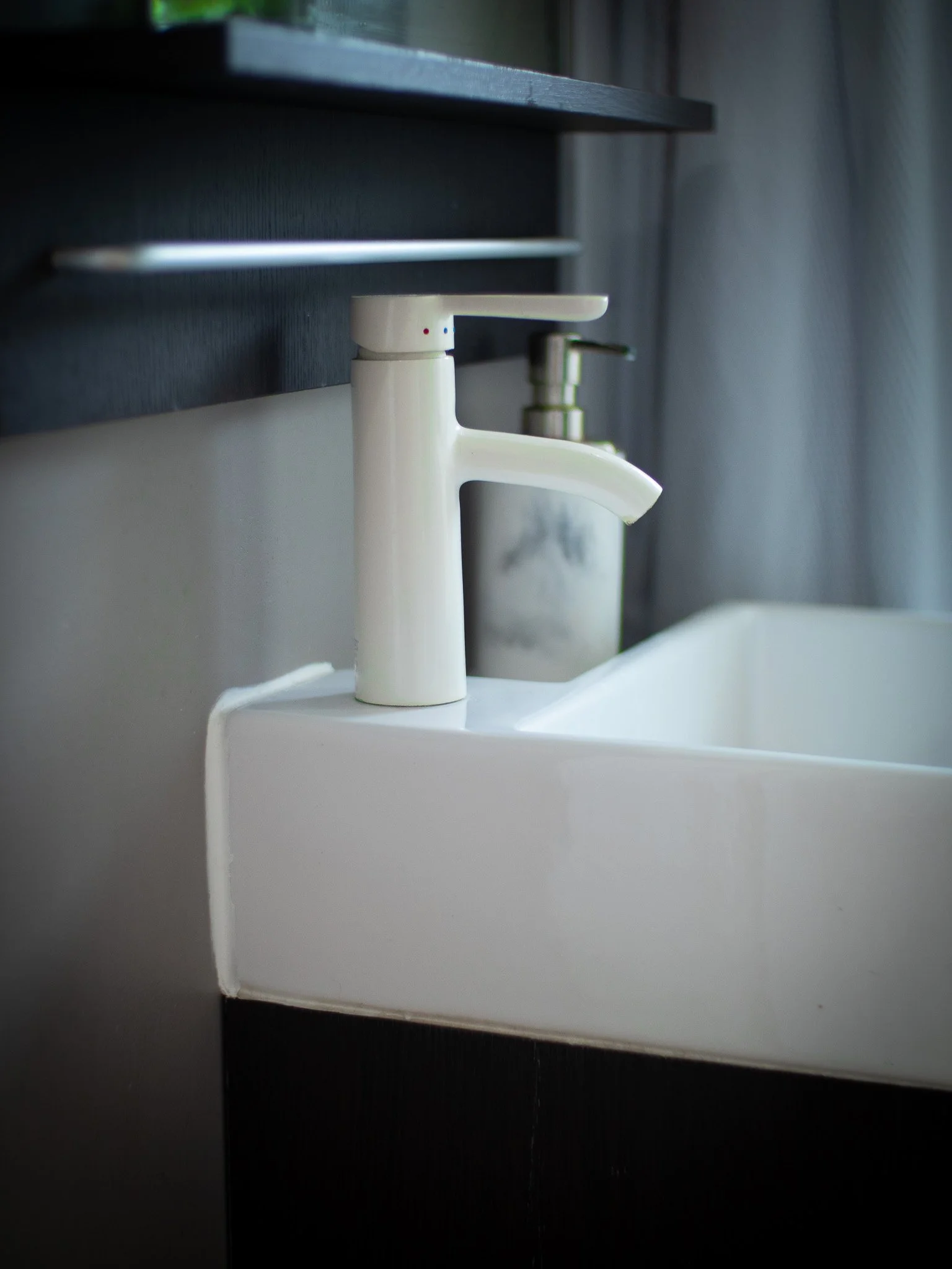 Close-up of a white bathroom sink faucet with a dark wall and countertop.