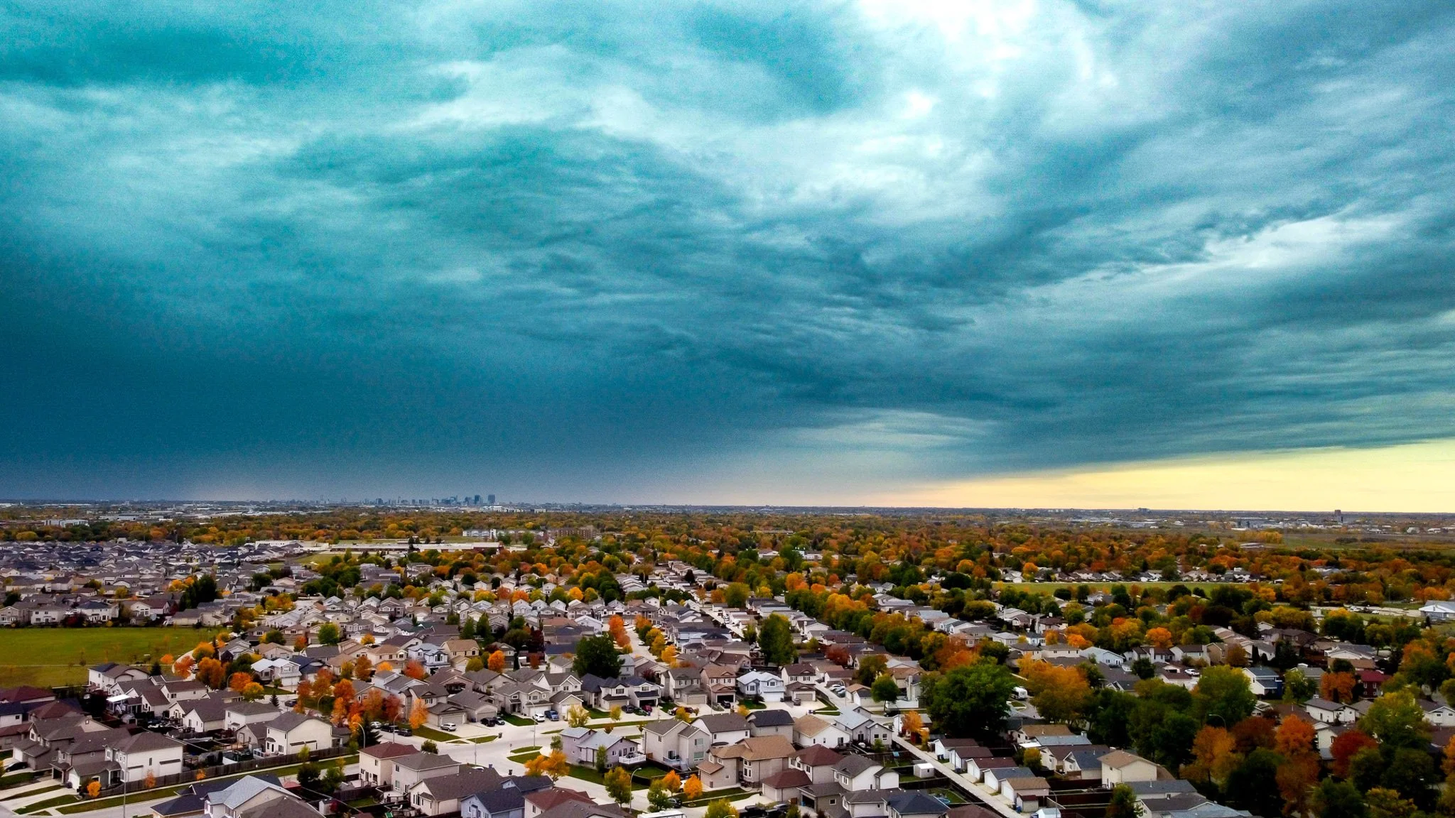 Aerial view of a suburban neighborhood with rows of houses and colorful trees, under a cloudy sky Winnipeg Manitoba.