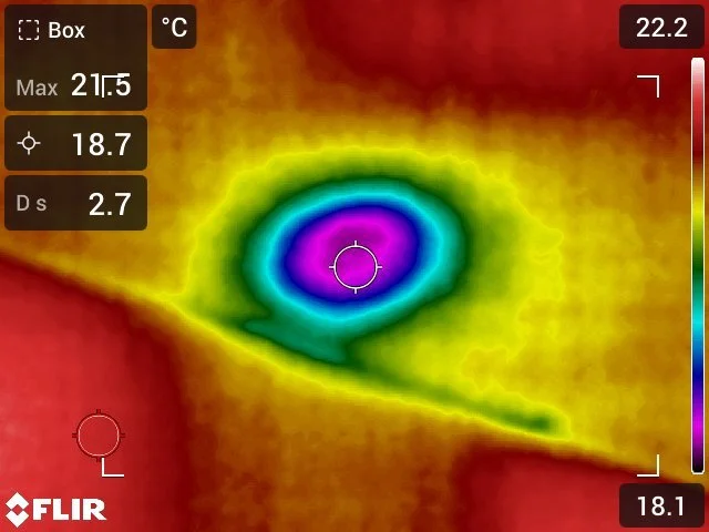 Infrared thermal image showing a circular hot spot with purple center, surrounded by blue, green, yellow, and red areas indicating decreasing heat levels, with temperature readings and a color scale.
