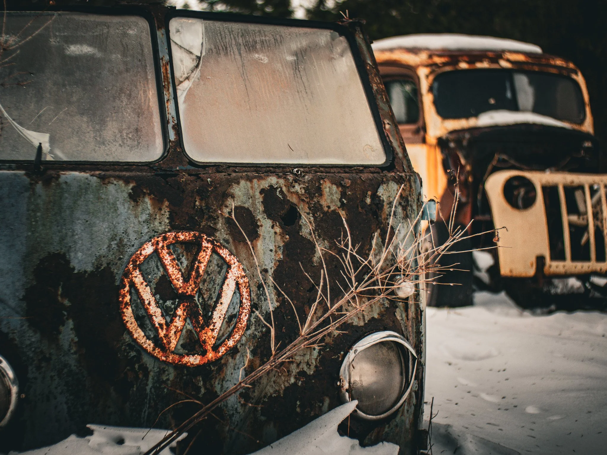 Close-up of an old, rusted Volkswagen van with a peeling logo, parked outdoors on snow with dry grass nearby, in a rural or deserted area Duncan BC Vancouver Island.
