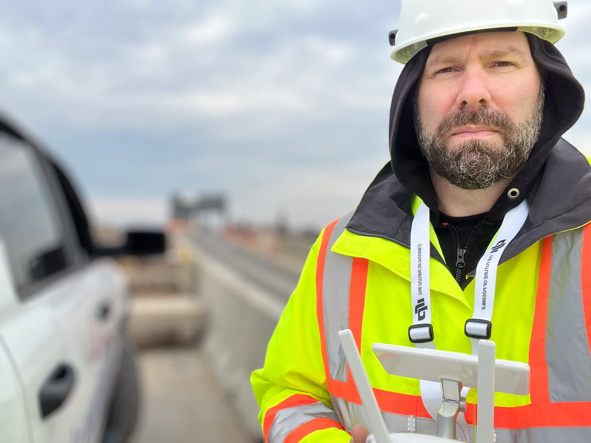 Construction surveyor wearing a white hard hat and high-visibility vest while using surveying equipment outdoors Stephen Spencer winnipeg 