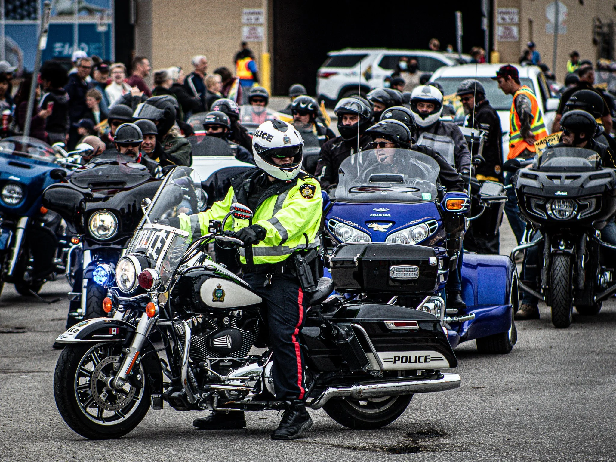 Police officer riding a motorcycle in a procession, with a crowd and police vehicles in the background ride for dad Winnipeg MB
