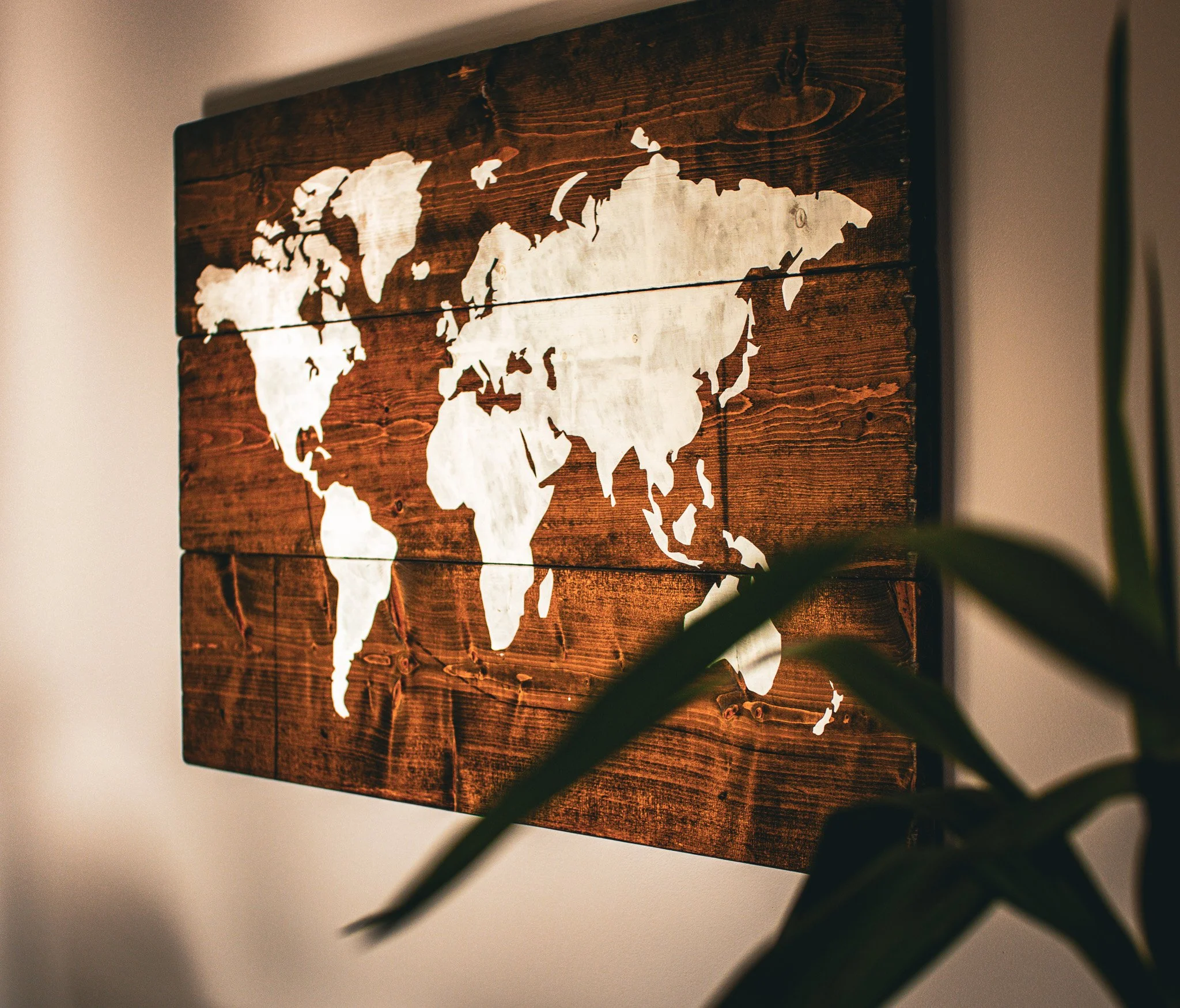 A wooden wall art piece featuring a cut-out world map silhouette, mounted on a wall with soft lighting.