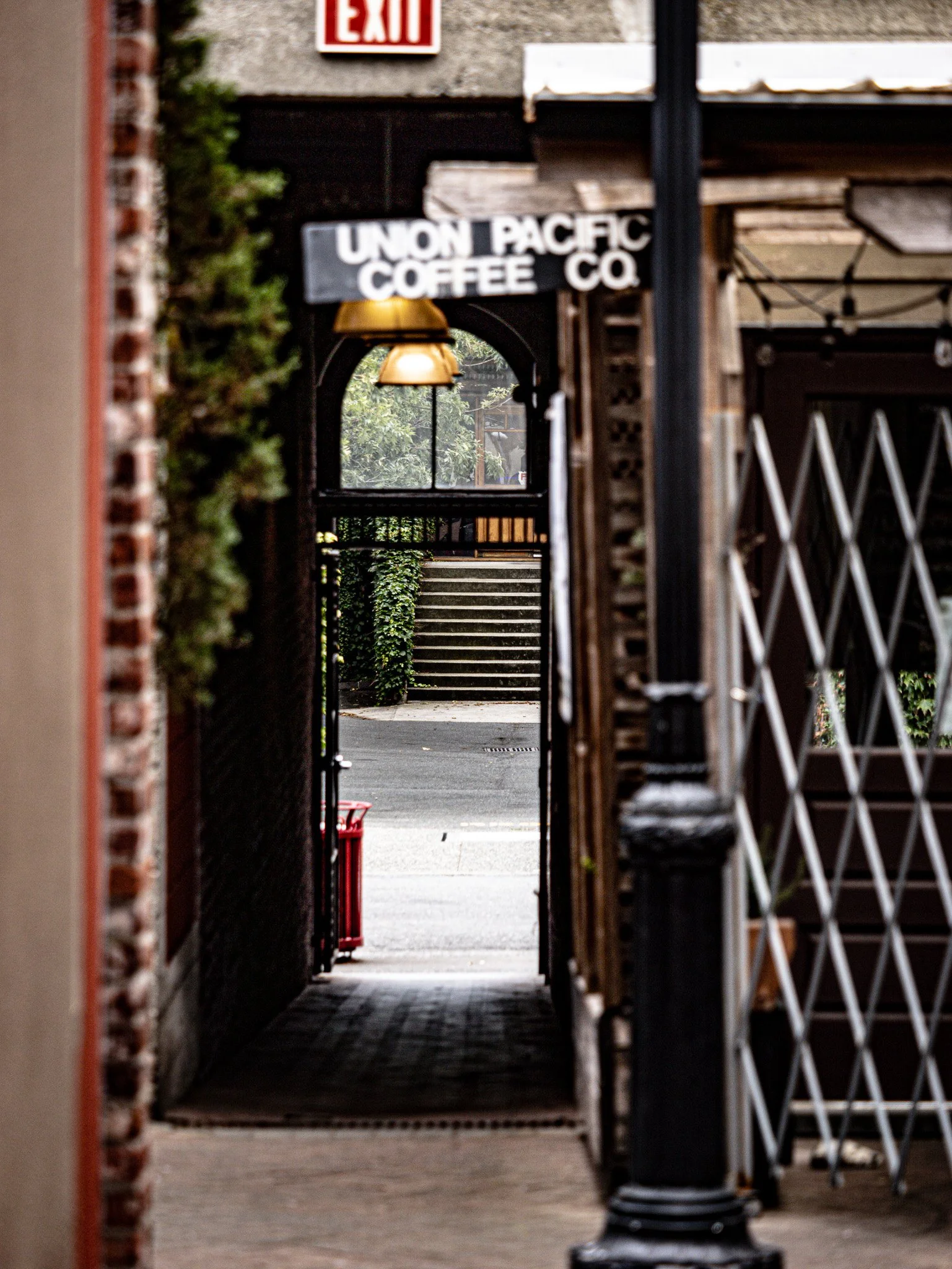 View through a narrow alley showing an outdoor staircase and greenery, with a sign for Union Pacific Coffee Company and an exit sign at the top