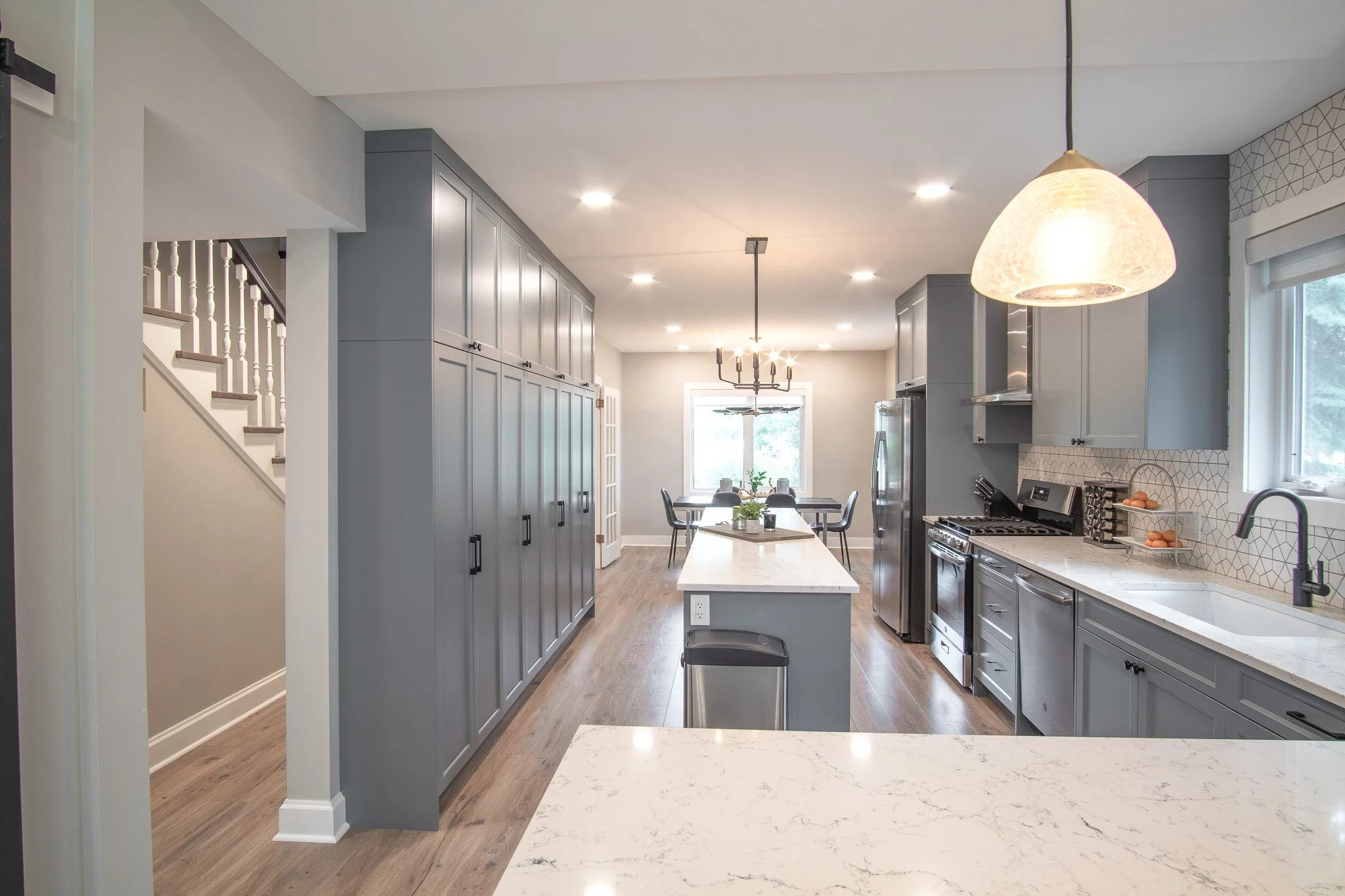 Modern kitchen with blue cabinetry, marble countertops, stainless steel appliances, and a dining area with a window and overhead lighting.