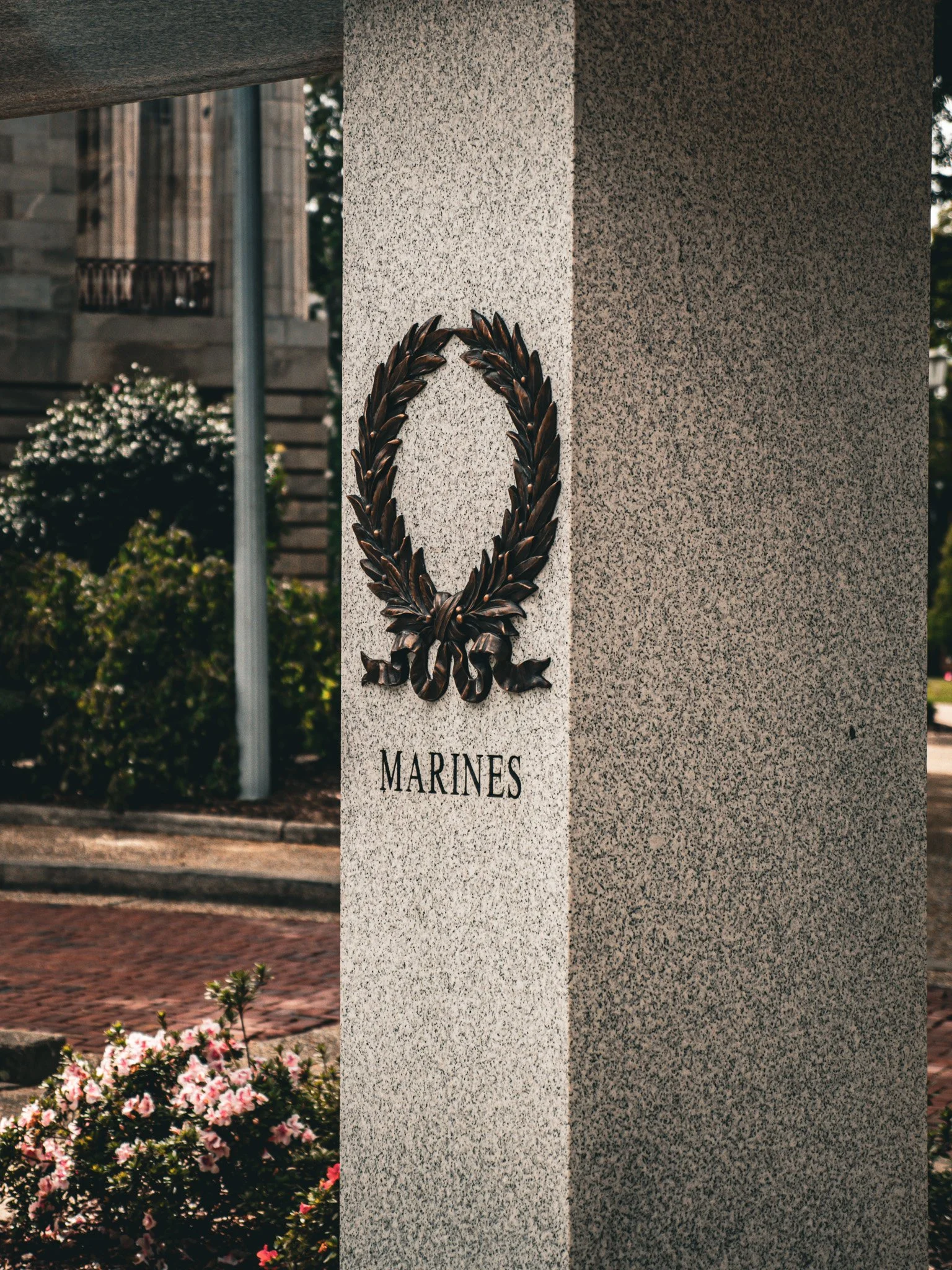 Memorial monument with a bronze wreath and the word 'MARINES' inscribed on it, outdoors with flowers and shrubs nearby North Carolina.
