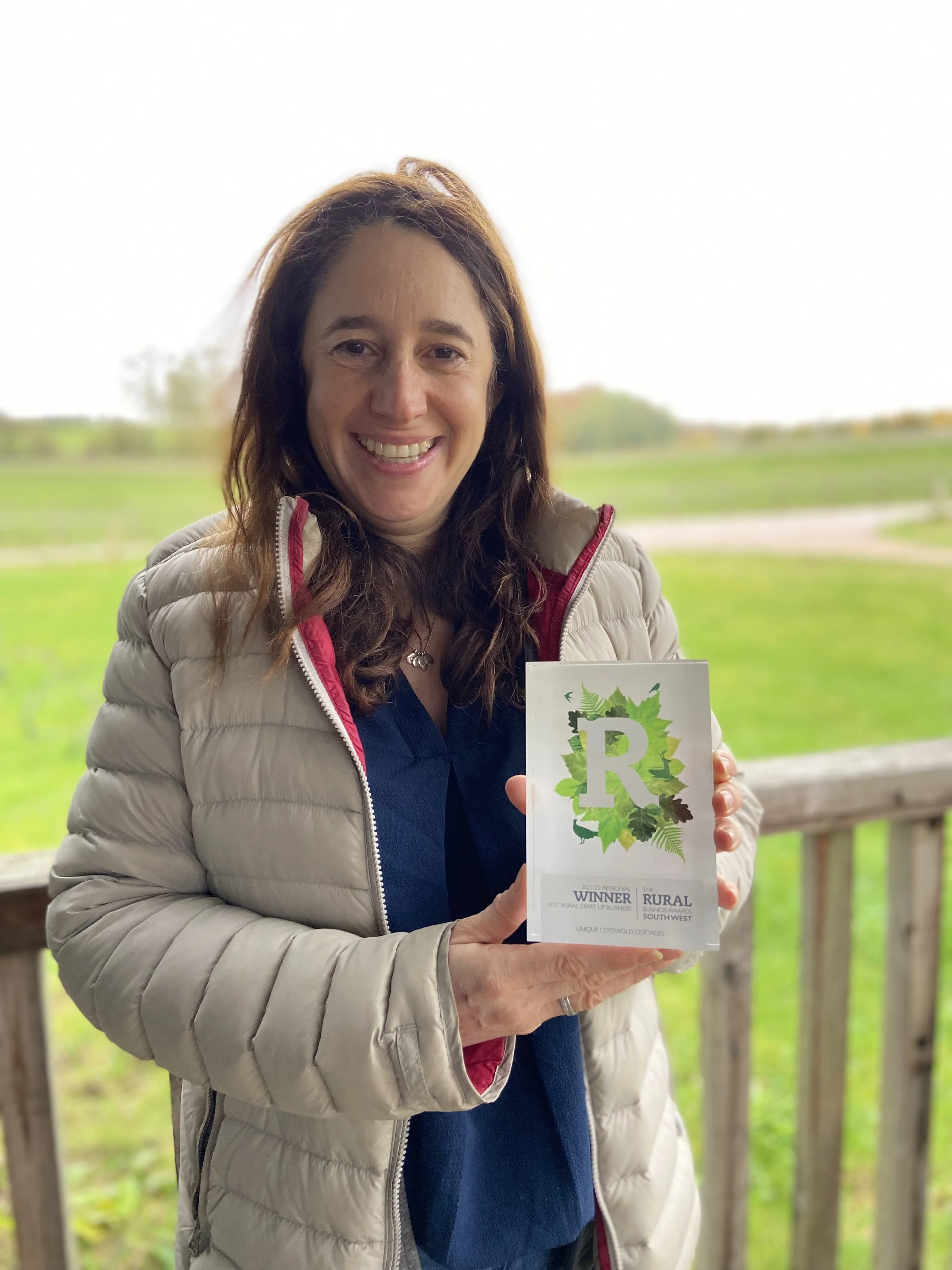 A portrait photograph of Amanda Stecker smiling outdoors while holding up her Rural Business Awards trophy on her website's Who Am I page