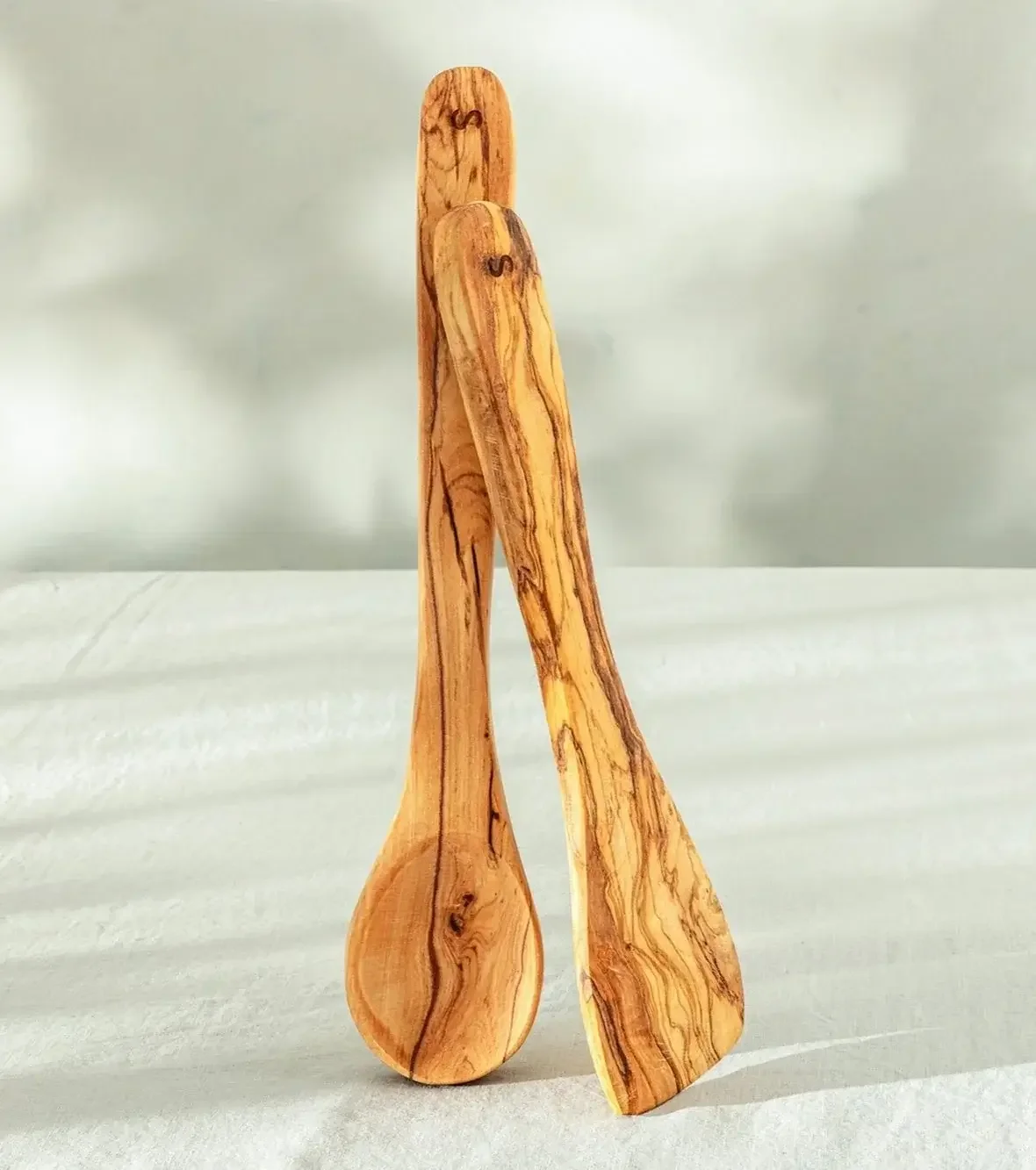 Two wooden kitchen utensils, a spoon and a spatula, leaning against each other on a light surface.