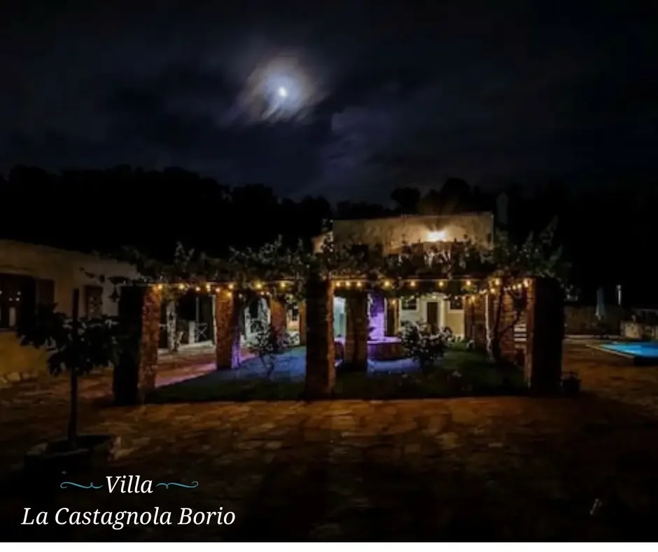 Nighttime view of Villa La Castagnola Borio with outdoor lighting, a patio area, and a cloudy moonlit sky.