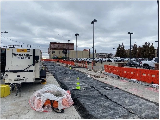 Image showing blankets covering a freshly poured track slab. Orange barricades can be seen protecting pedestrians from the work zone.