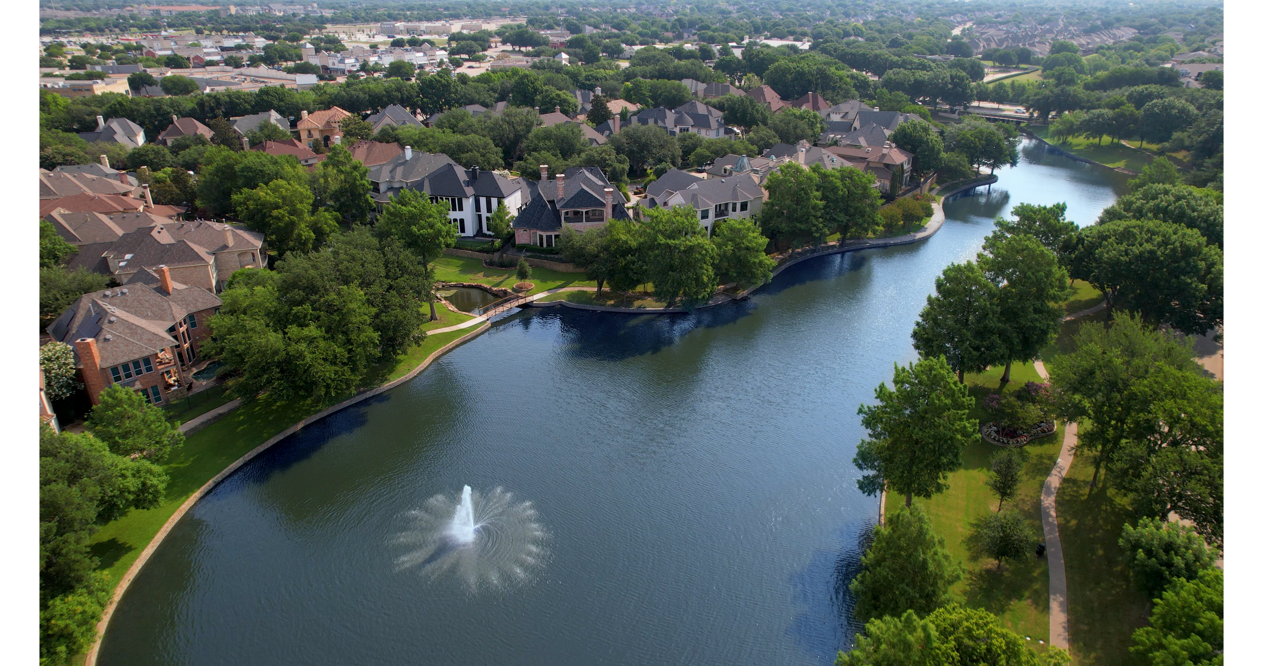 Aerial view of a luxury West Plano neighborhood with tree-lined homes along a lake