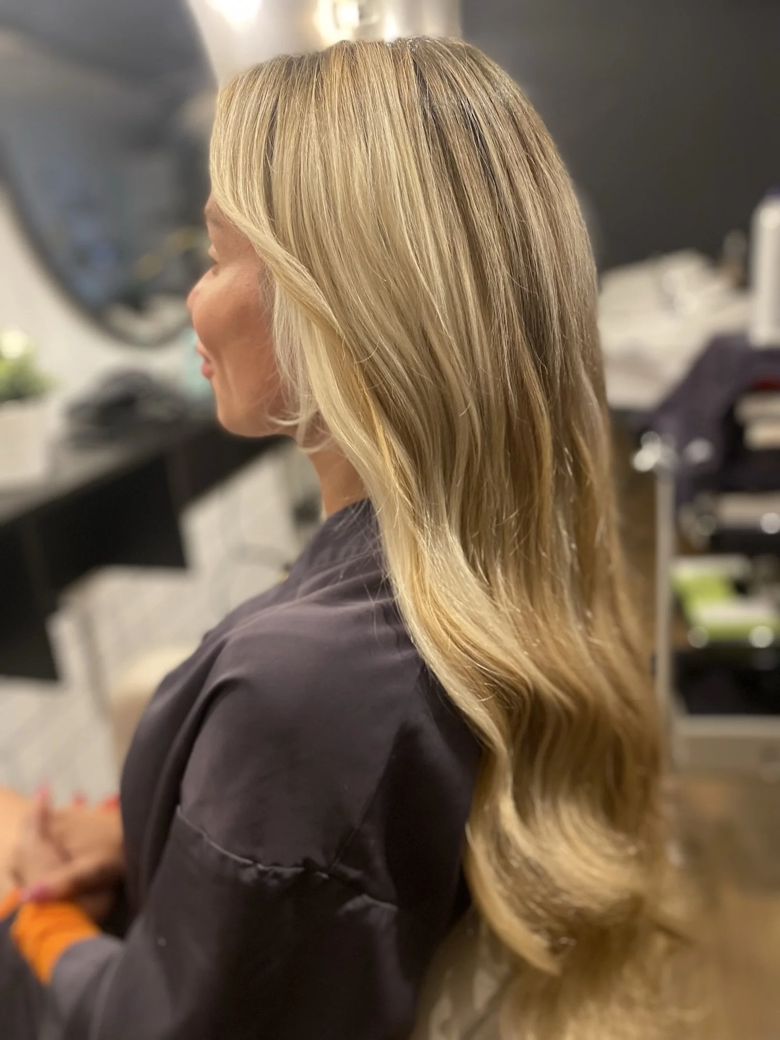Side view of a woman with long, wavy blonde hair in a hair salon.