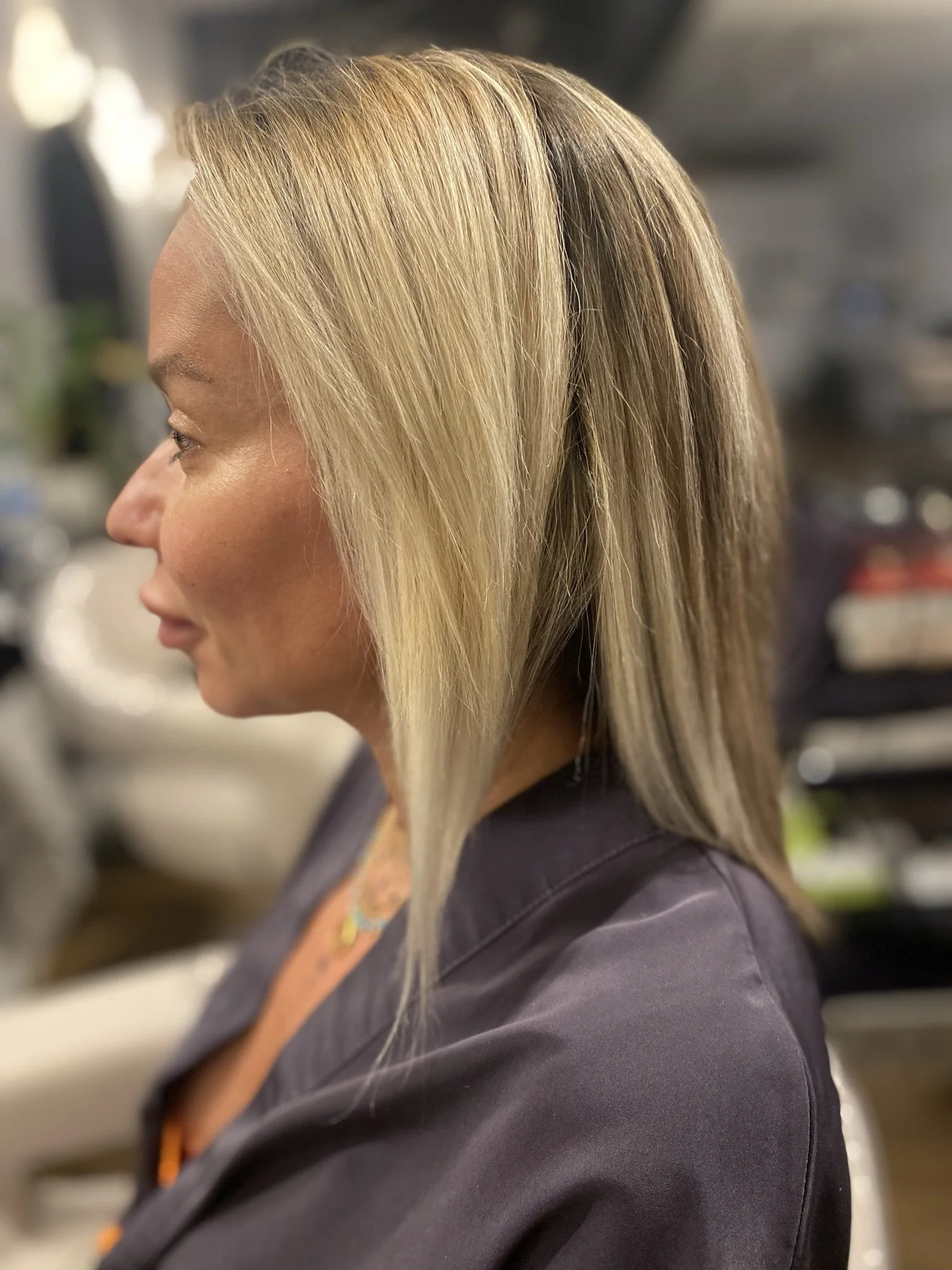 Side view of a woman with shoulder-length blonde hair and a dark gray top, sitting in a hair salon.