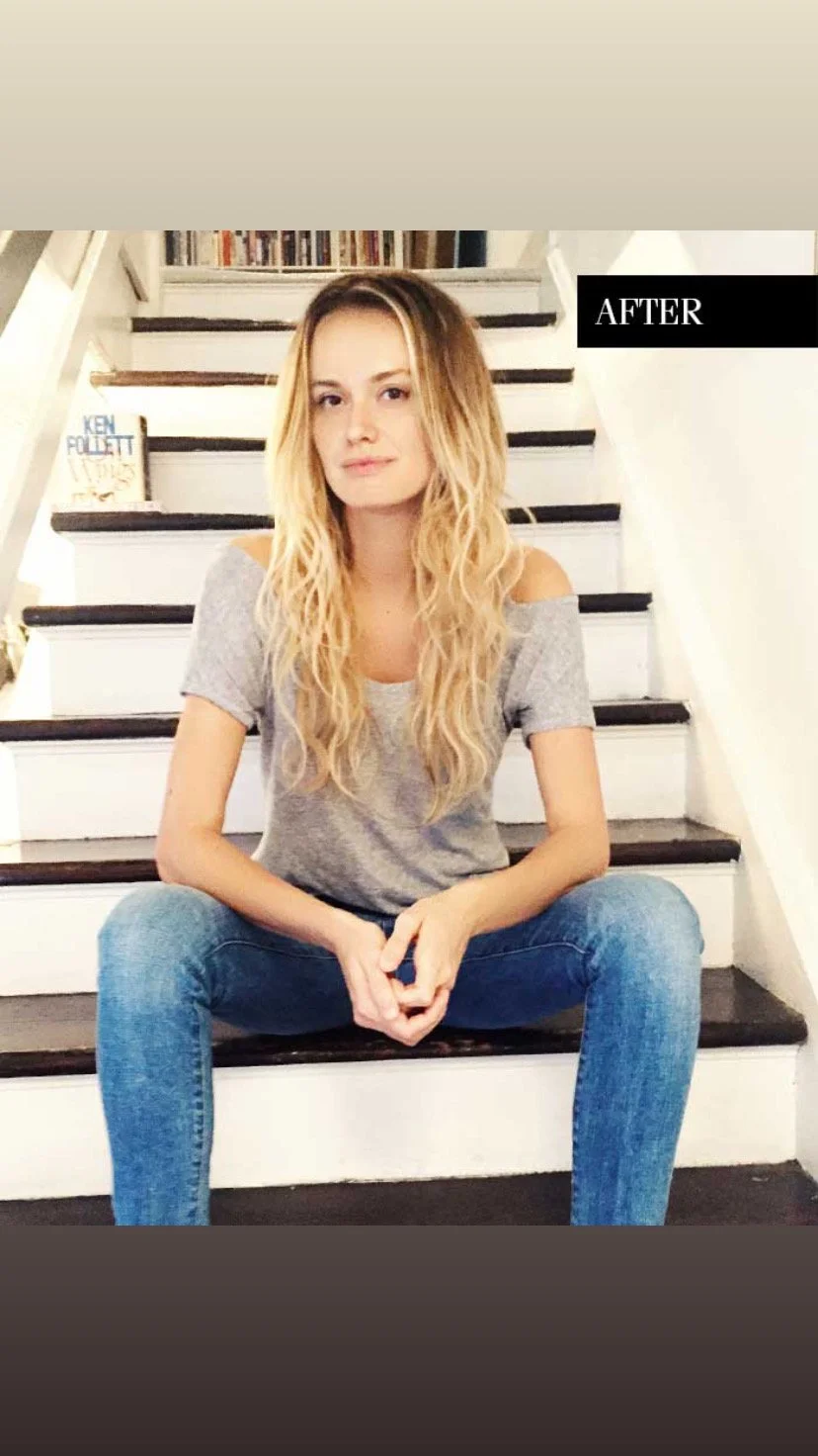 A young woman with long, wavy blonde hair, wearing a gray off-shoulder t-shirt and blue jeans, sitting on black and white stairs indoors. There is a book titled 'Ken Follett' on a shelf behind her, and the word 'AFTER' is written on the top right cor
