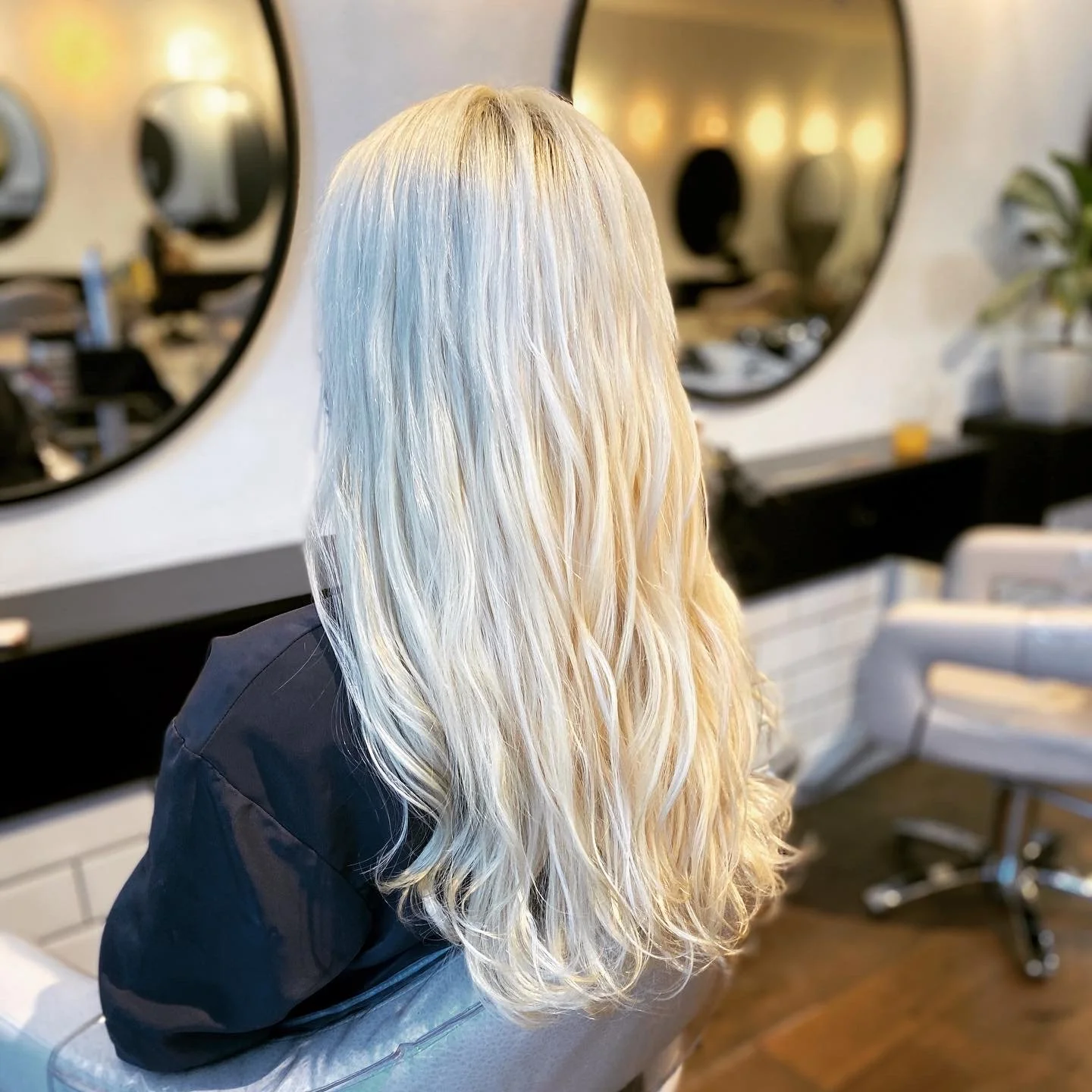 Blonde wavy hair on person sitting in a salon chair with mirrors and salon equipment in the background.