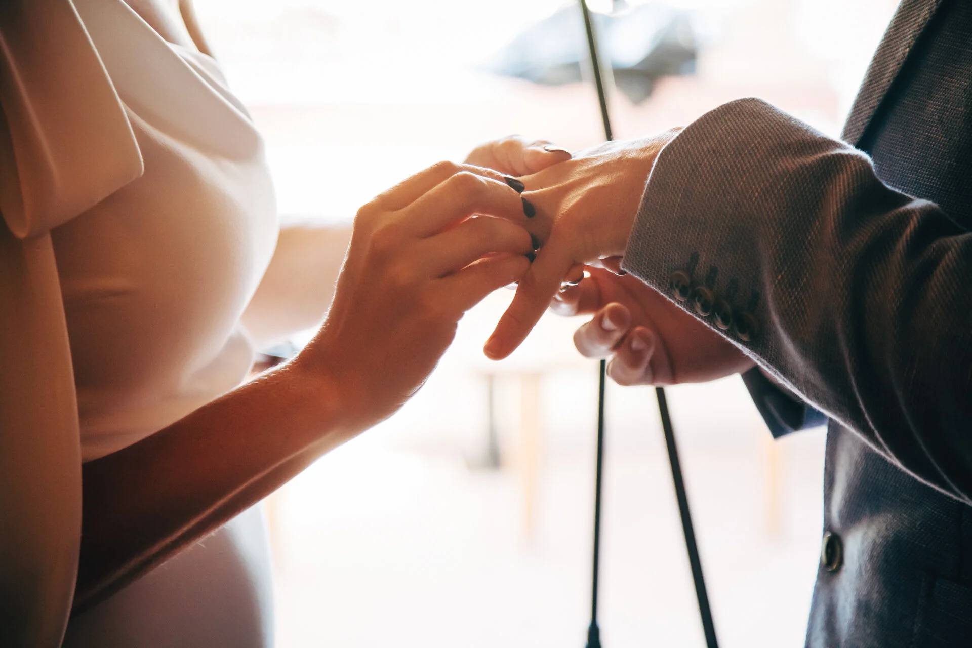 A close-up of a woman placing a ring on a man's finger during a wedding or engagement ceremony.