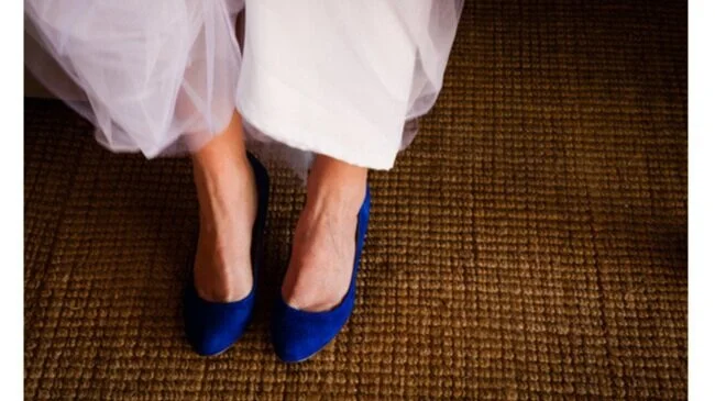 Close-up of a person wearing blue shoes and a white dress, standing on a brown carpeted floor.