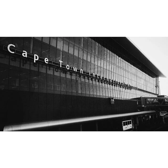 Black and white photo of Cape Town International Airport's modern glass facade with its name partially visible.