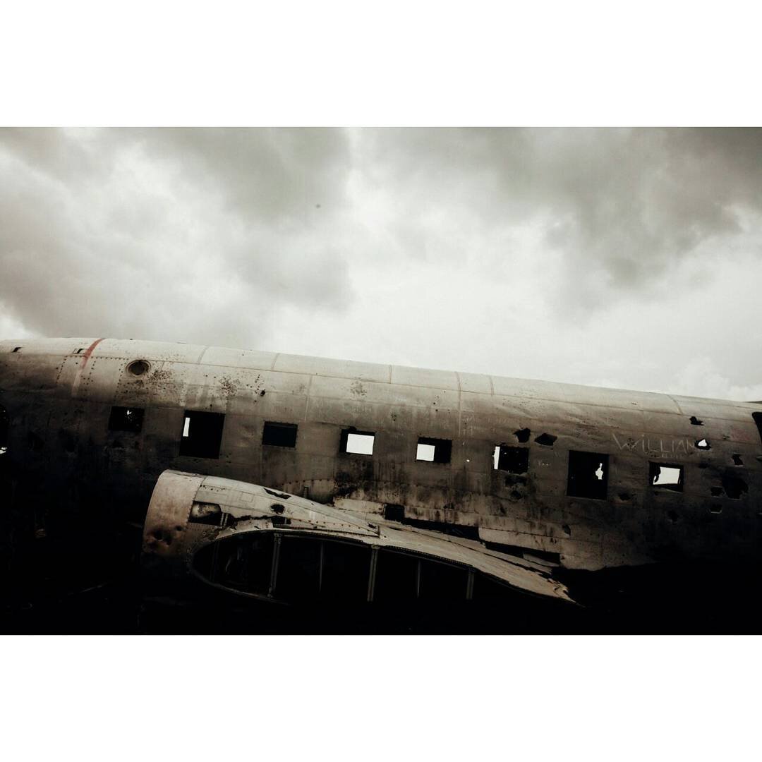 A wreckage of an abandoned airplane in Iceland with broken windows and damaged metal fuselage under a cloudy sky.