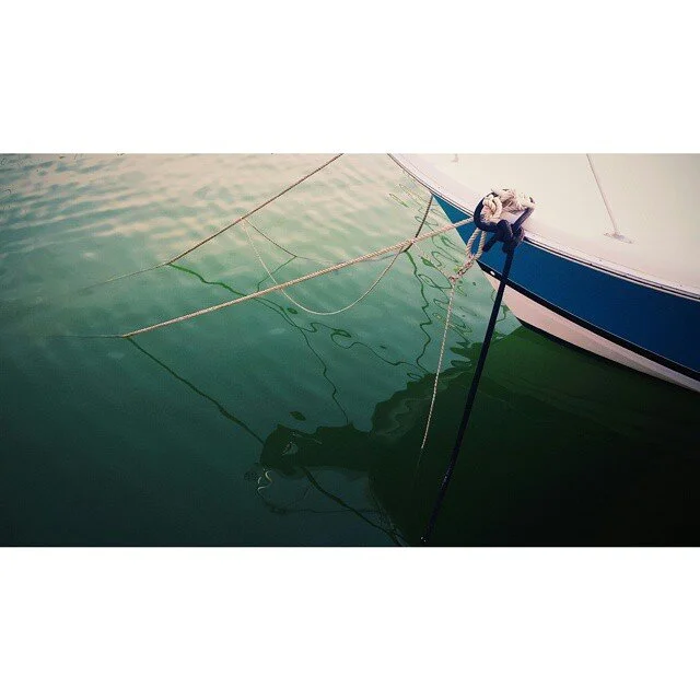Part of a boat anchored in calm water, with ropes and the boat's bow visible.