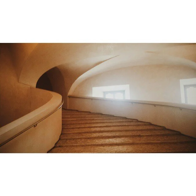 Curving stairs inside a building, with white walls and two windows emitting light.