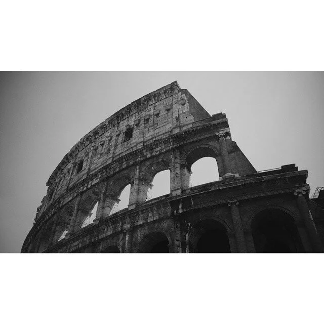Black and white photo of the Colosseum in Rome, Italy, from a low angle.