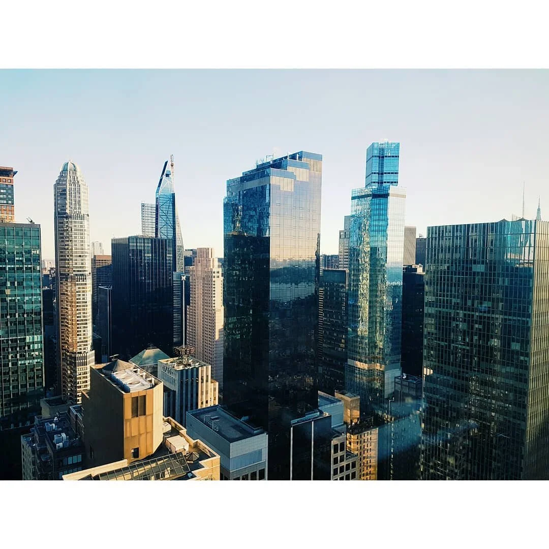 New York cityscape of tall skyscrapers with reflective glass windows, city streets below, under a clear blue sky.