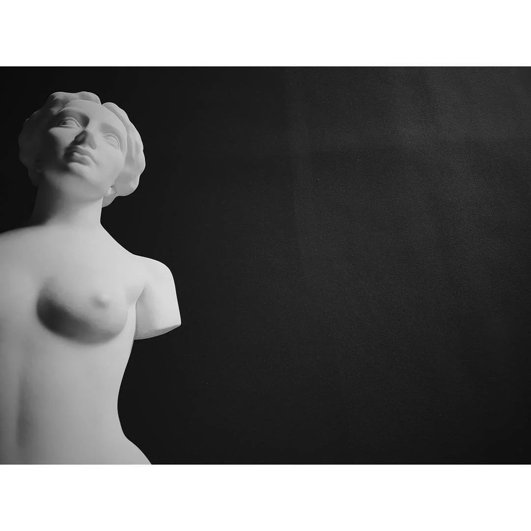 Black and white photo of a classical sculpture of a female figure against a dark background.