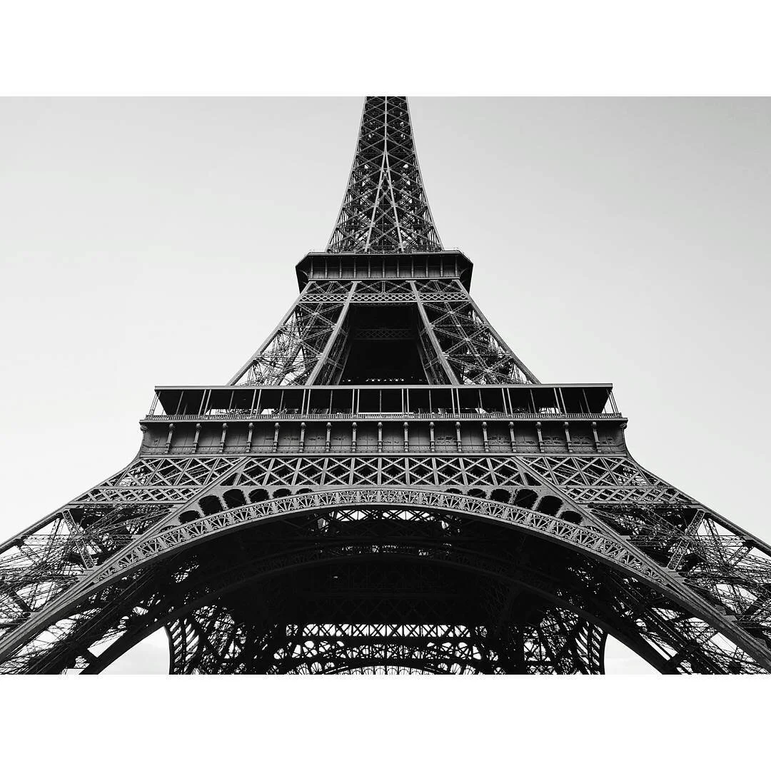 Black and white photo of the Eiffel Tower taken from below, showcasing its intricate iron lattice structure.