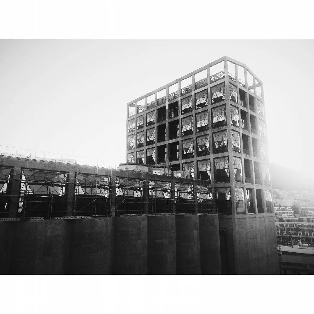 Black and white photo of a modern multi-story building with scaffolding in front, featuring large glass windows and geometric architectural design.