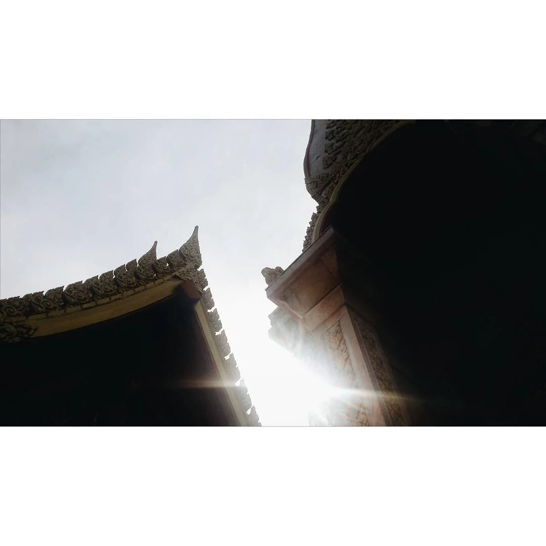 Sunlight shines between traditional ornate rooftops of a temple or palace with intricate carving details.