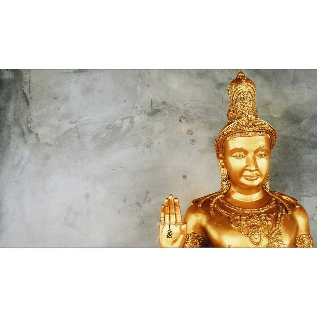 Gold-colored Hindu deity statue with a peaceful expression, ornate crown, and jewelry, positioned against a plain wall.