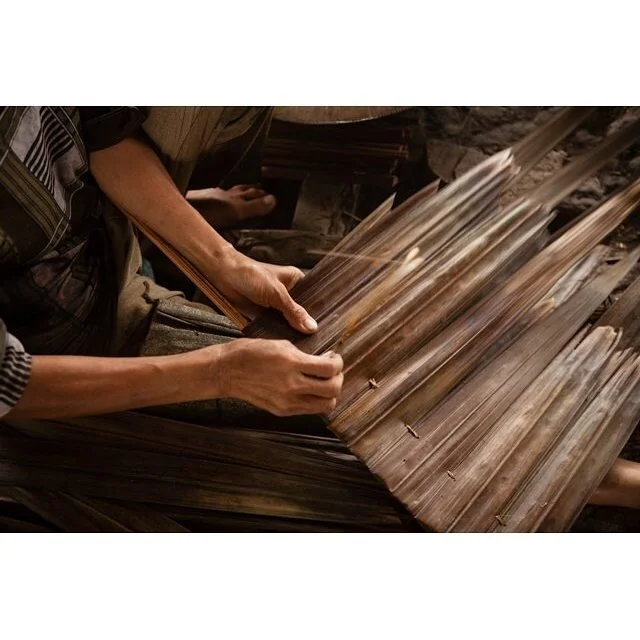 Person weaving a basket with natural brown palm leaves or similar material.