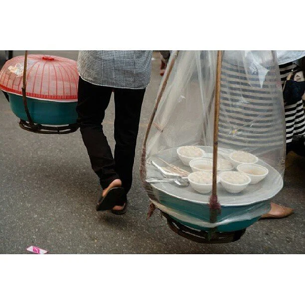 Person walking on street carrying two large containers with bowls of food, one container has a transparent cover.