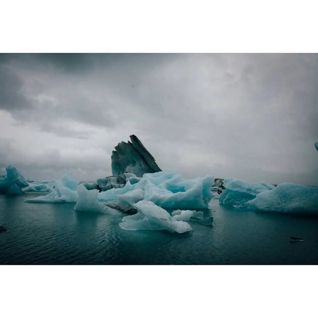 Icebergs floating in the ocean under a cloudy sky.