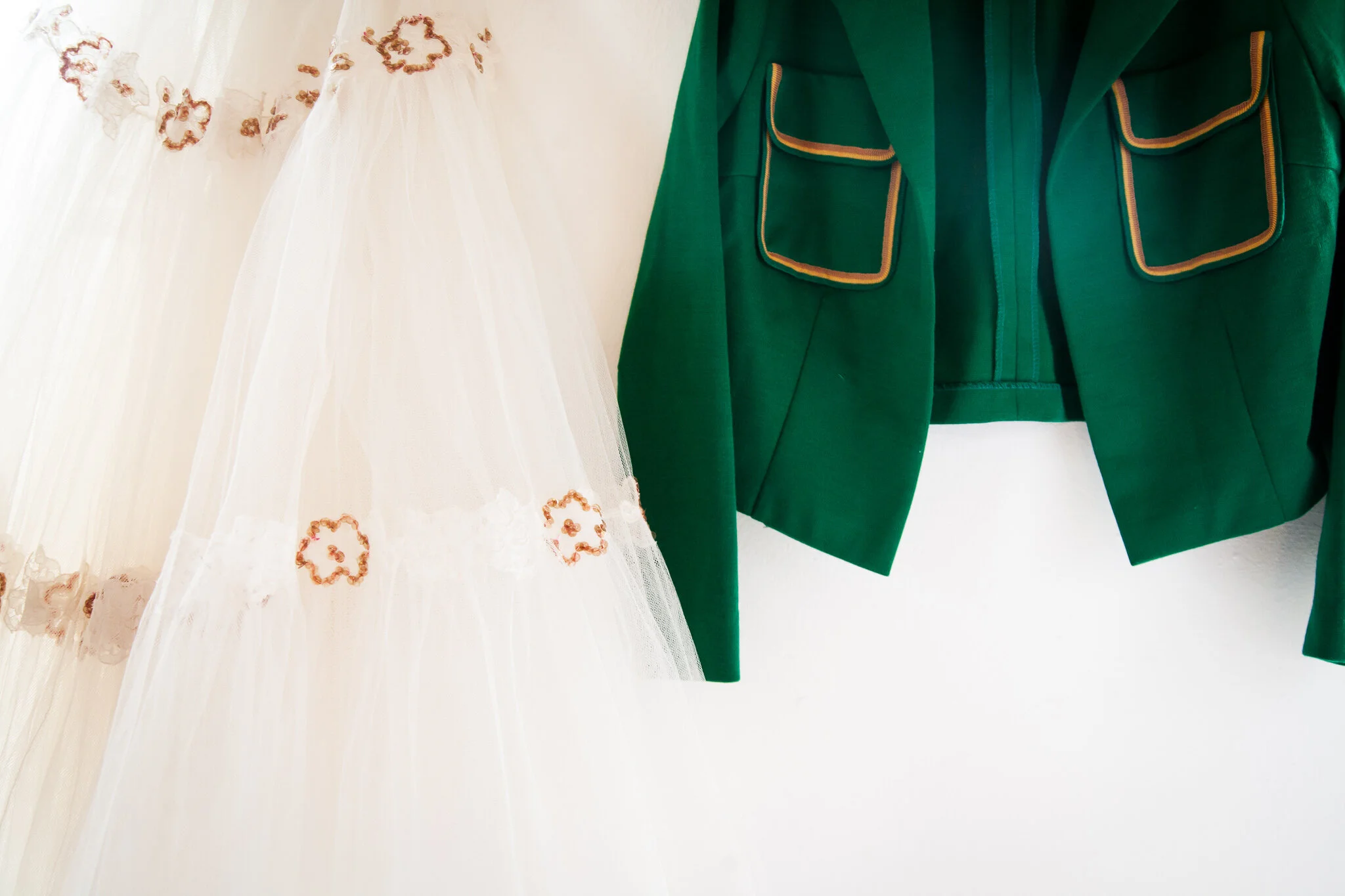 Close-up of a wedding dress with floral embroidery and a green jacket with yellow trim.
