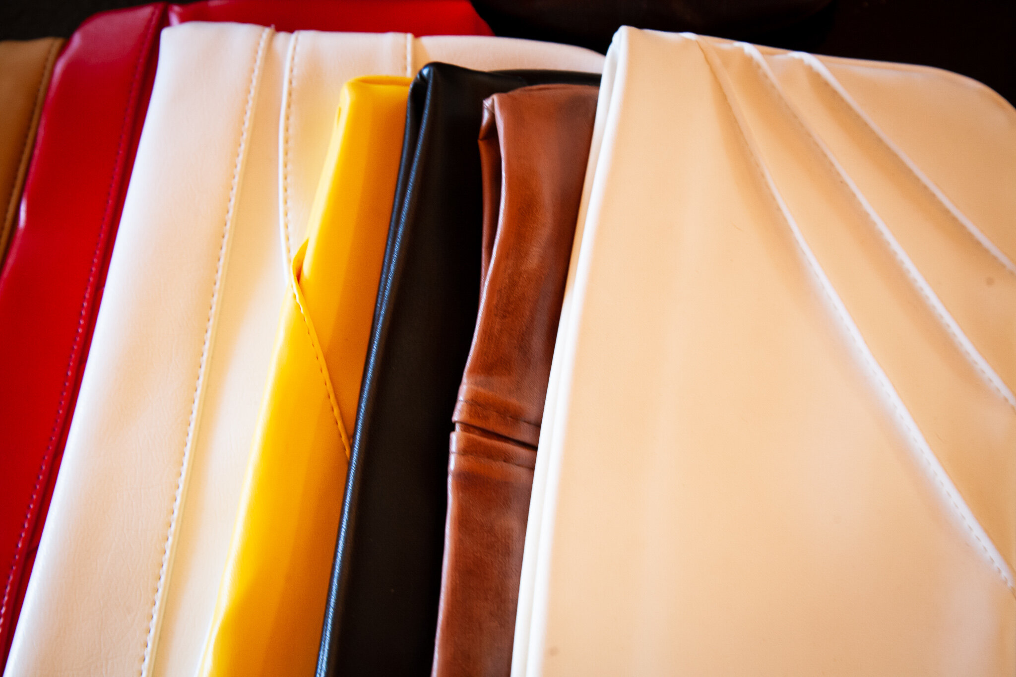 Close-up of various colorful leather or faux leather bags or wallets, including red, white, yellow, black, brown, and beige, arranged side by side.