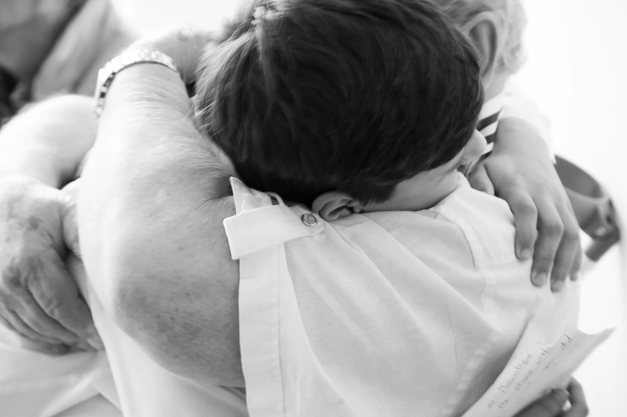 A child hugging a grandfather, with the child's face turned into the person's shoulder.