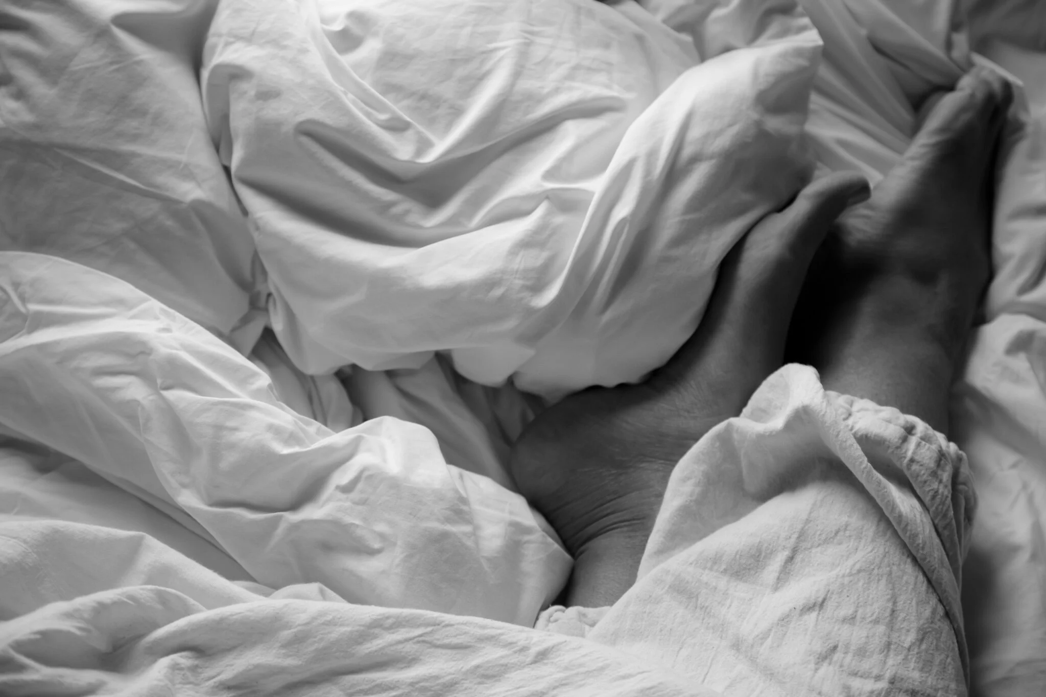 Close-up of a person's hand holding another person's hand on a bed with white sheets.